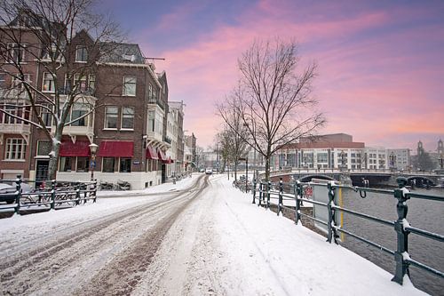 Besneeuwd Amsterdam aan de Amstel in de winter bij zonsondergang in Nederland