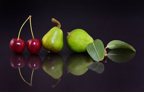 Pears and cherries are reflected against a dark background