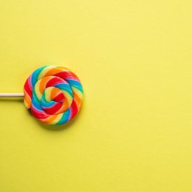 Rainbow colours on a lollipop against a bright yellow background – cheerful children’s and food photography by Christa Stroo photography