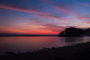 Silhouetted reflecting rock at sunset on a sand beach