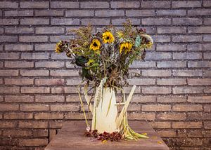 eine alte Gießkanne mit getrockneten Sonnenblumen an einer Außenwand e einst helle, jetzt sterbende 