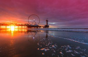 La jetée de Scheveningen et la grande roue se reflètent dans le sable mouillé et le rouge d'une belle soirée.
