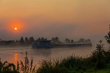 een vrachtschip tijdens zonsopkomst over de maas in de mist