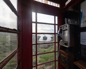 Peek through old phone booth with boat visible through windows
