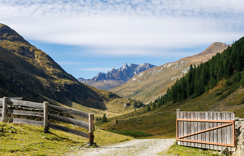An open wooden gate offering sweeping views of the high Alpine valley