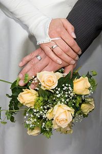 Mains d'un couple de mariés sur le bouquet de la mariée