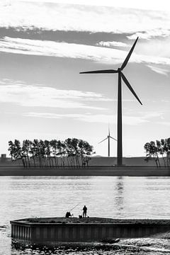 Silhouettes of a lone fisherman and wind turbines in backlight. (portrait shot) by John Duurkoop