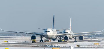 Een Lufthansa Airbus A330 en een Air China Boeing 777 worden gesleept naar de terminal. van Jaap van den Berg