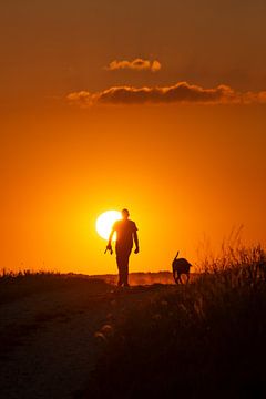 Man with dog in sunset by J. Einmahl