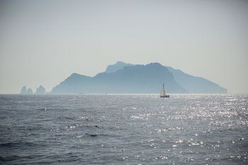 A sailboat sails off an island on the Amalfi coast in Italy