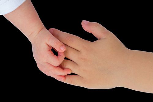 Hand of baby touching hand of child on black