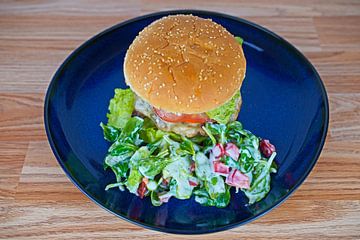 Cheeseburger met veldsla garnituur geserveerd op een blauw bord