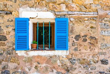 Detailopname van stenen muur en raam met blauwe luiken van huis van Alex Winter