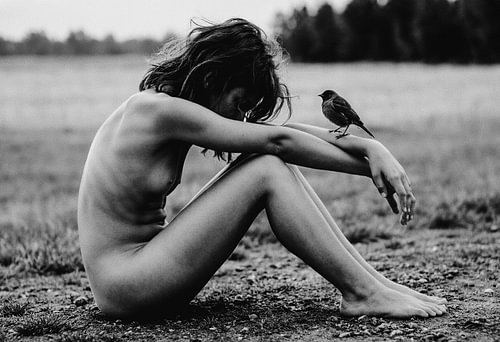 Nackte Frau mit Vogel in offener Landschaft