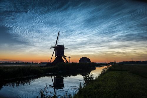 Lichtende nachtwolken boven een windmolen in het hollandse landschap