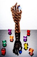 Hölzerne Hand, die einen blauen Würfel zwischen Daumen und Zeigefinger hält, umgeben von 8 mehrfarbigen Würfeln.