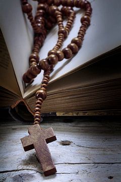 katholische Holz-Rosenkranzperlen mit Kreuz in einem alten Buch über rustikales Altholz, religiöses 