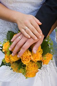 Mains d'un couple de mariés sur le bouquet de la mariée