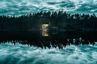 Illuminating cabin on reflecting lake with dramatic sky