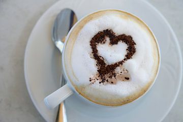 kopje cappuccino met cacaopoeder in hartvorm op een tafel in een straatcafé, hooghoekig zicht van bo van Maren Winter