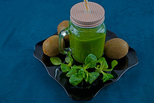 Leaf salad and kiwi smoothie on black plate decorated with kiwi and field salad
