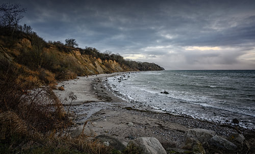 Steilküste mit Strand, Steinen und Wellen unter dunklem Wolkenhimmel an der Ostsee in Mecklenburg-Vo