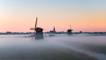 Foggy sunrise with morning glow, classic mills and a church near Schermhorn