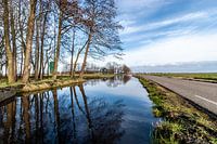 Polder landscape with high water in the canal. Windless weather sky reflects blue in the water
