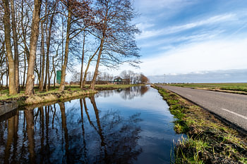 Polderlandschap met hoog water in de vaart. Windstil weer lucht spiegelt blauw in het water