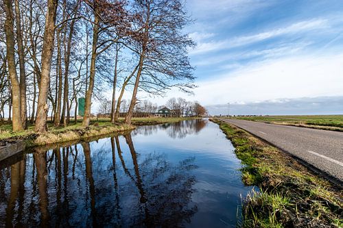 Polderlandschap met hoog water in de vaart. Windstil weer lucht spiegelt blauw in het water