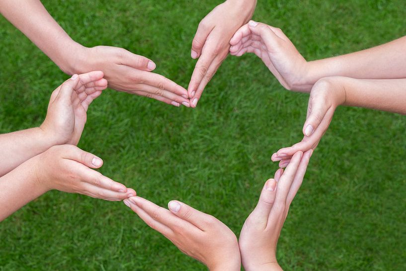 Many arms and hands of girls make heart shape over  grass by Ben Schonewille