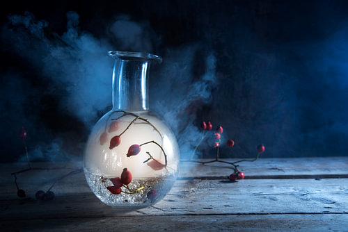 Flasche mit glühendem Rauch und Hagebutten im Inneren auf einem rustikalen Holztisch vor dunkelblaue