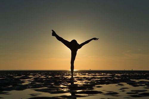 Artistiek naakt op de waddenzee op 1 been in een propeller pose