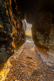 Blick zwischen Kalksteinfelsen an der Küste der Normandie bei Sonnenuntergang mit warmem Abendlicht und einem trockengelegten Strand von Bram Lubbers