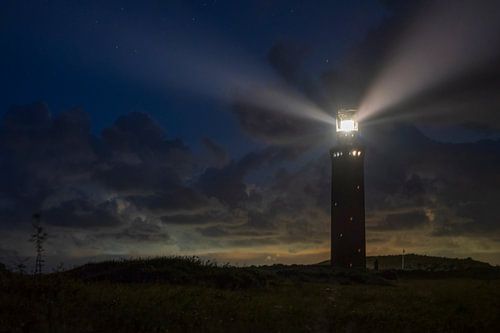 Vuurtoren in de duinen met lichtbundels bij nacht
