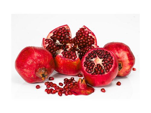 Een levendige robijnrode oogst: Verse granaatappels, heel en geopend, barstend van de sappige zaadjes op wit
