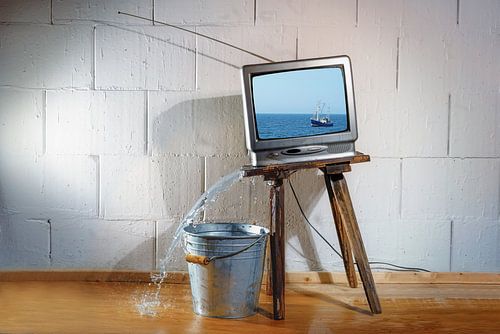 Un vieux téléviseur vintage posé sur un tabouret en bois incliné montre un film sur un bateau.  sur Maren Winter