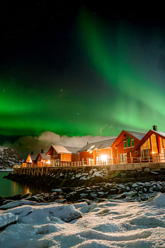 Aurore boréale au-dessus des cabanes de pêcheurs rouges dans la neige à Lofoten, Norvège
