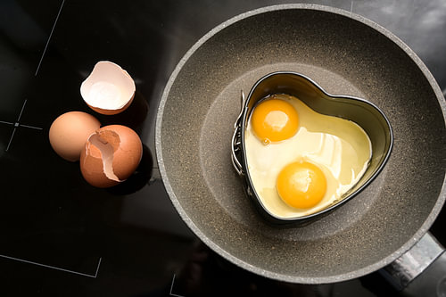 Zwei Spiegeleier in Herzform auf einer Bratpfanne und leere Schalen auf dem schwarzen Herd, Kochen m