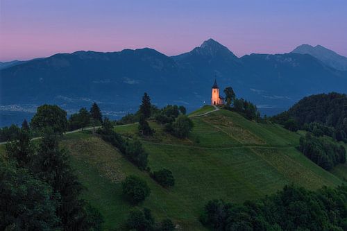 Het kerkje van Jamnik in Slovenië na zonsondergang - panoramafoto van het Alpenlandschap