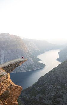 Une personne est assise sur la Trolltunga en Norvège au coucher du soleil