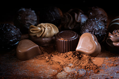 Schokoladenpralinen und Kakaopulver auf rustikalem Holz als Liebesgeschenk, Nahaufnahme vor dunklem 