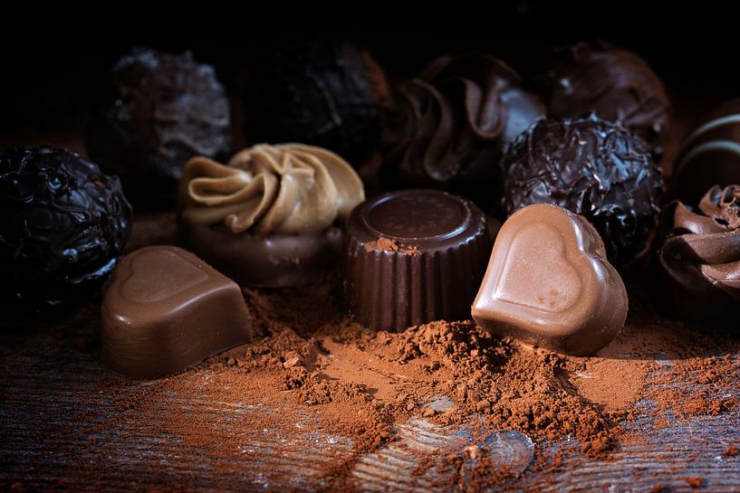 Chocolate pralines and cocoa powder on rustic wood as a love gift, close up against a dark backgroun by Maren Winter