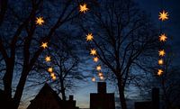 Verlichte Herrnhuter Moravische Kerststerren die boven de donkere silhouetten van oude huisgevels en van Maren Winter thumbnail