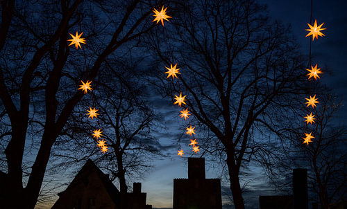 Beleuchtete Herrnhuter mährische Weihnachtssterne, die über den dunklen Silhouetten alter Hausgiebel