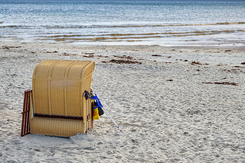 Strandkorb mit Krücken daran gelehnt im Sand am Meer, Sommerurlaub von Menschen mit besonderen Bedür