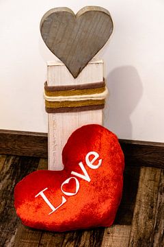 Ein Rotes Stoff Herz liegt vor einem Herz aus Holz von Tom Voelz