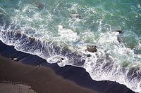 Wellen kräuseln sich auf schwarzem Strand