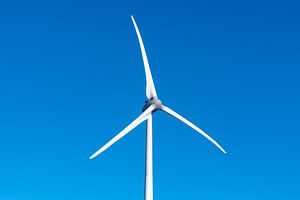 Windturbine mit sich drehenden Flügeln und blauem Himmel im Hintergrund