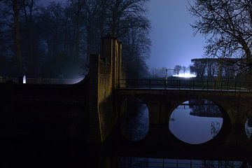 Een stenen brug over een gracht in de nacht